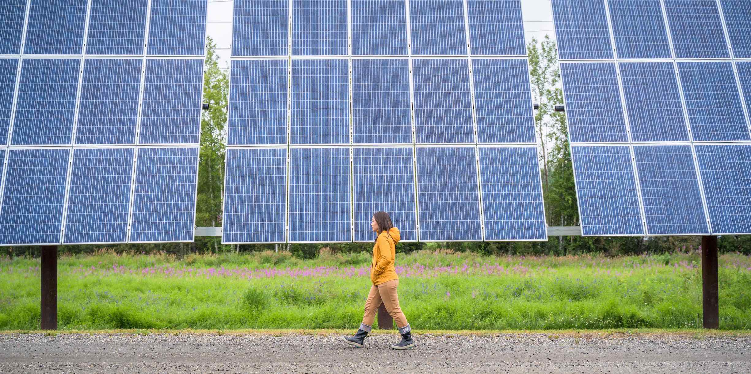 A woman walks in front of solar panels at the Cold Climate Housing Research Center. ​​Photo by Jeffrey Fisher, Alaska Center for Energy and Power 