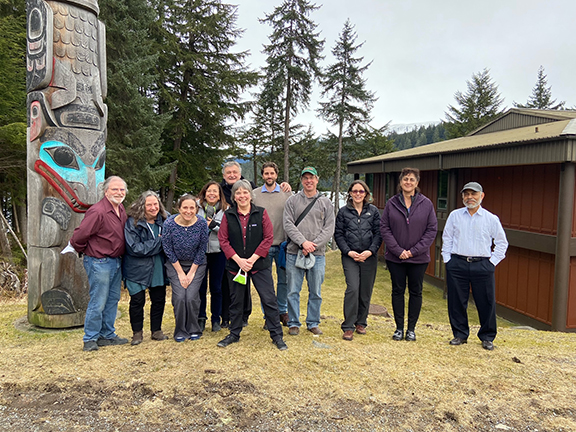 faculty alliance members stand together in front of a totem pole on green grass