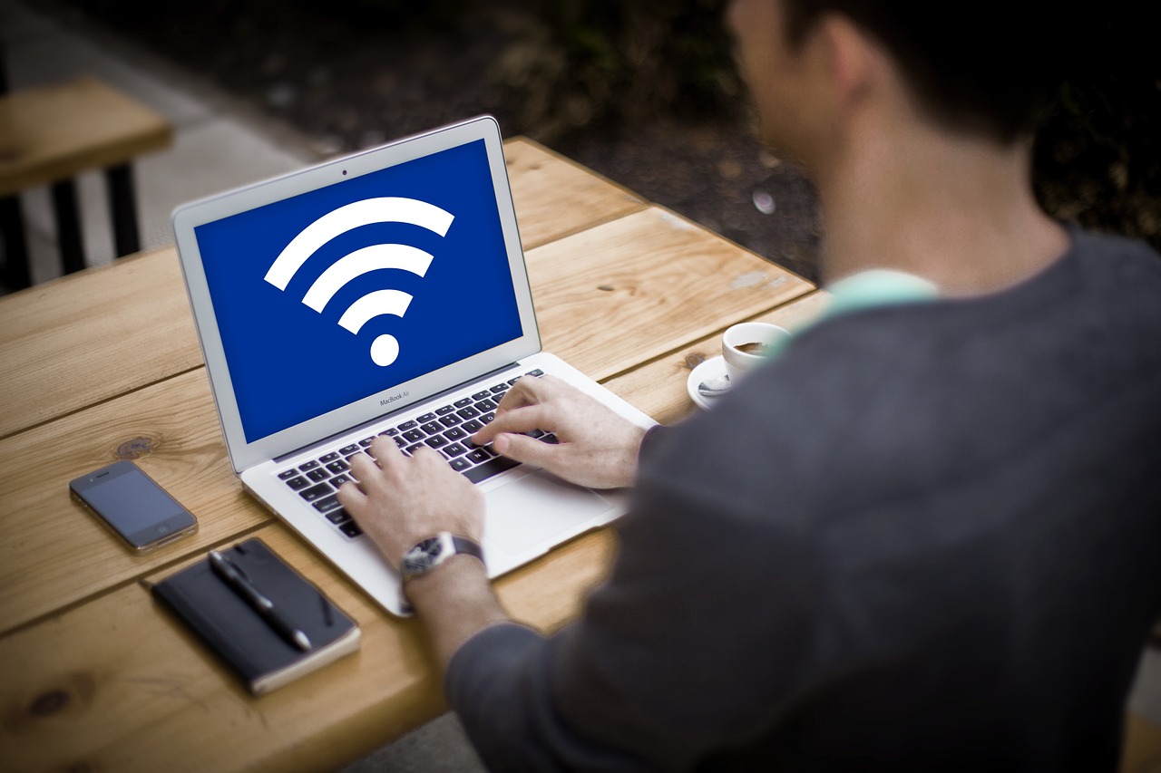 the back of a man working on a laptop with a large wifi symbol on his screen