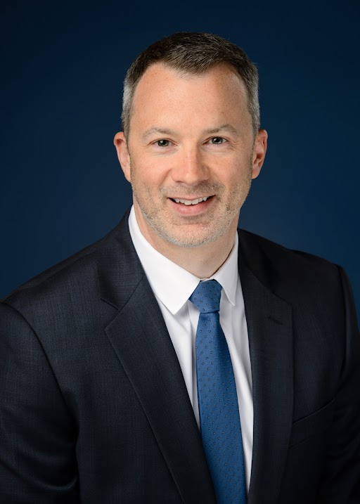 Luke Fulp Headshot, blue background, man with short hair smiling at camera