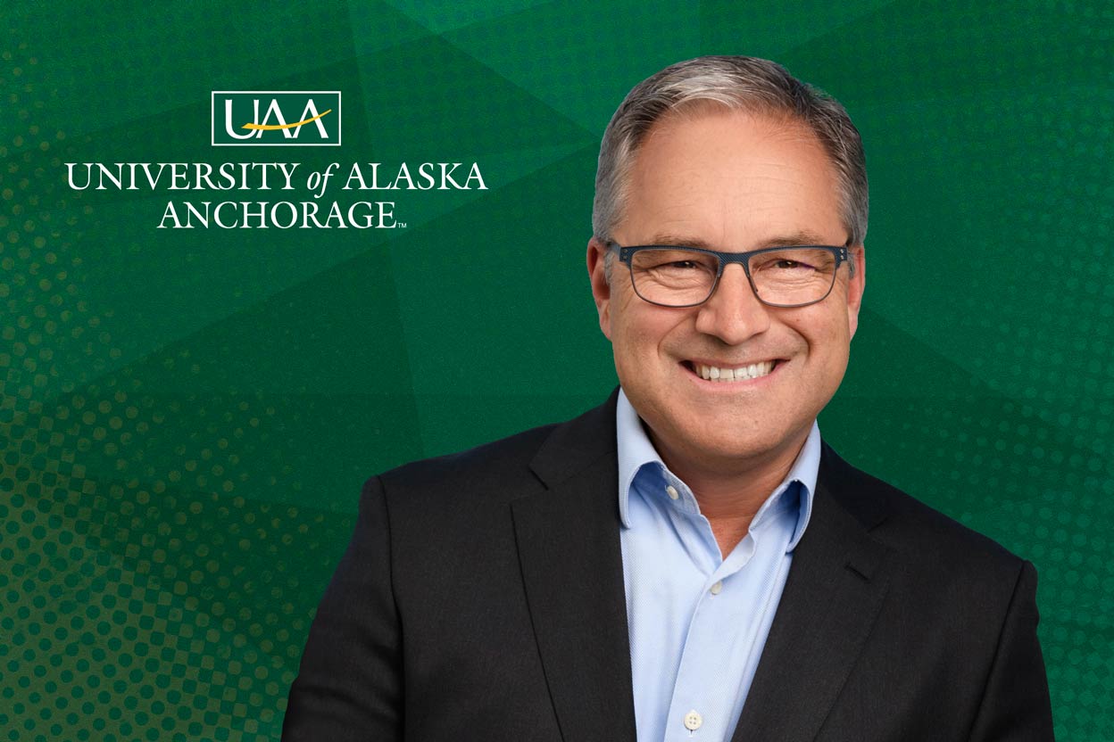 A man smiles in front of a green background that reads 