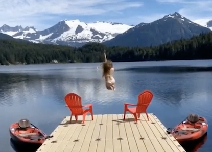 Screenshot from UAS day in the life UA/alaska travel TikTok promotion - a student jumps off a dock into Auke Lake on a clear day. Snowy mountains in the distance.