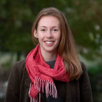 Amy Holt smiling outdoors in a red scarf and brown coat.
