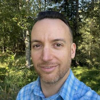 Colin Maher smiling outdoors in a blue plaid shirt.