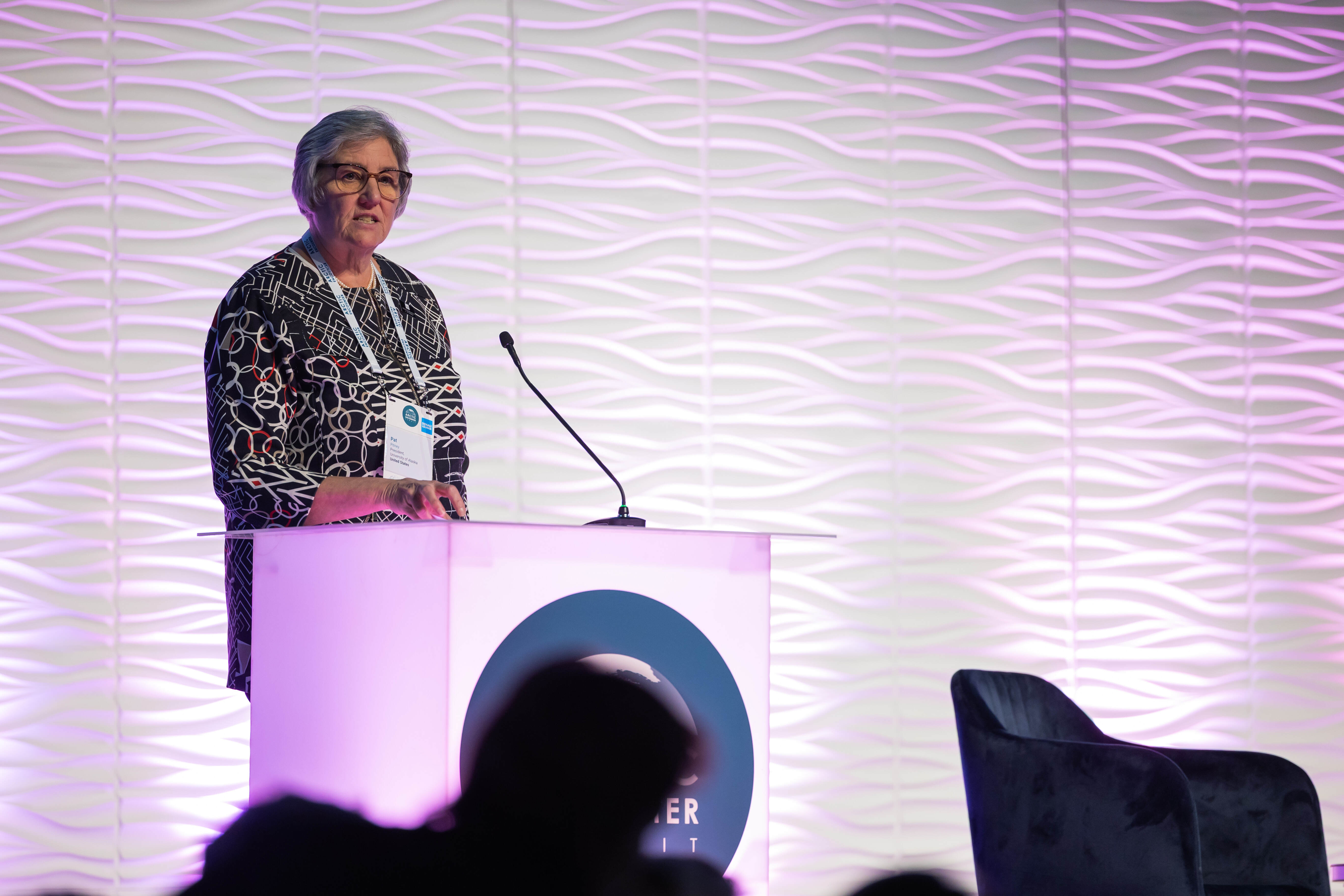 UA President Pat Pitney speaking at the Arctic Encounter Summit podium against the AES wave-pattern backdrop.