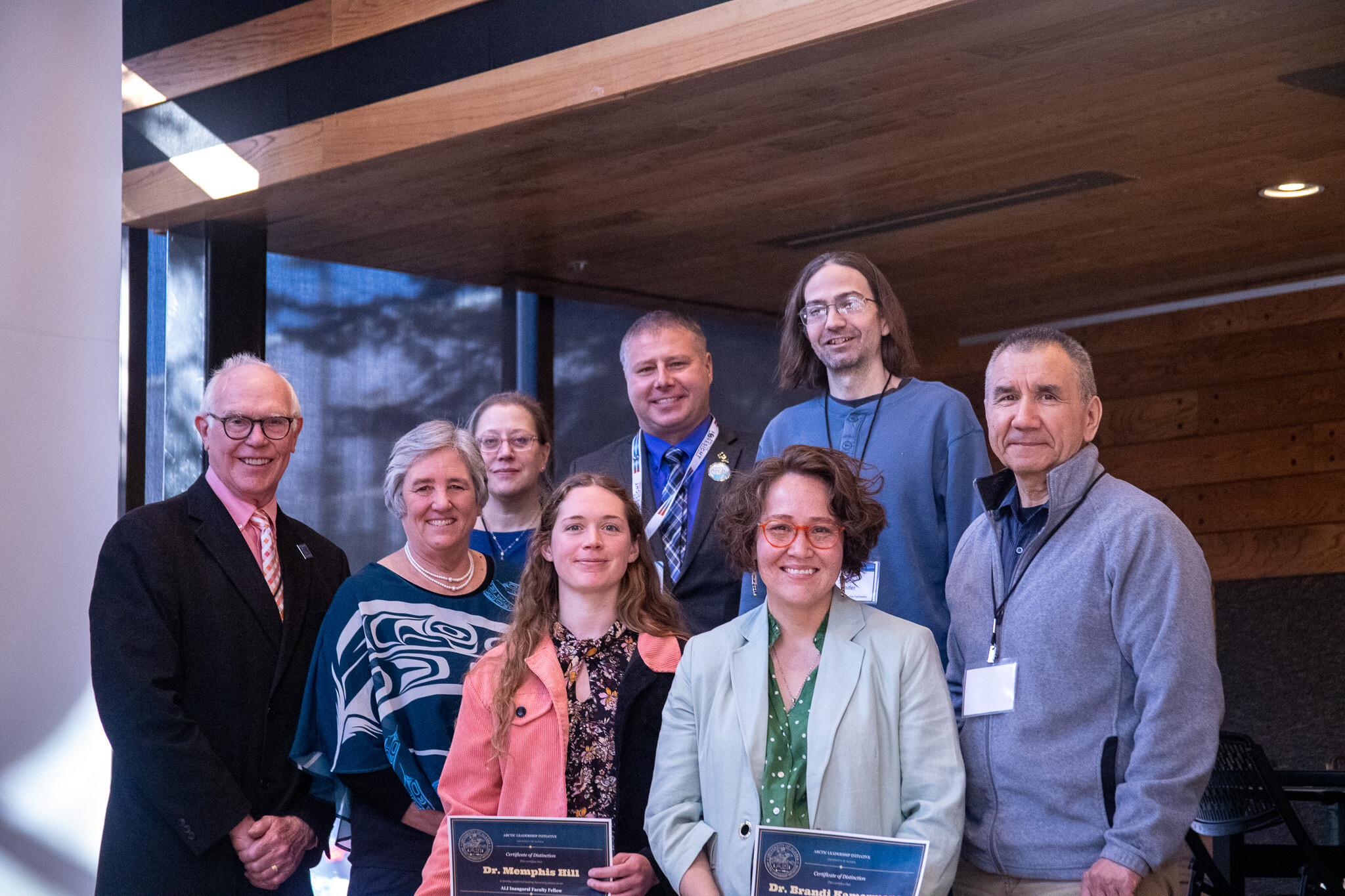 Group of nine people at the UAA Den, two front-and-center holding ALI Certificates of Distinction.