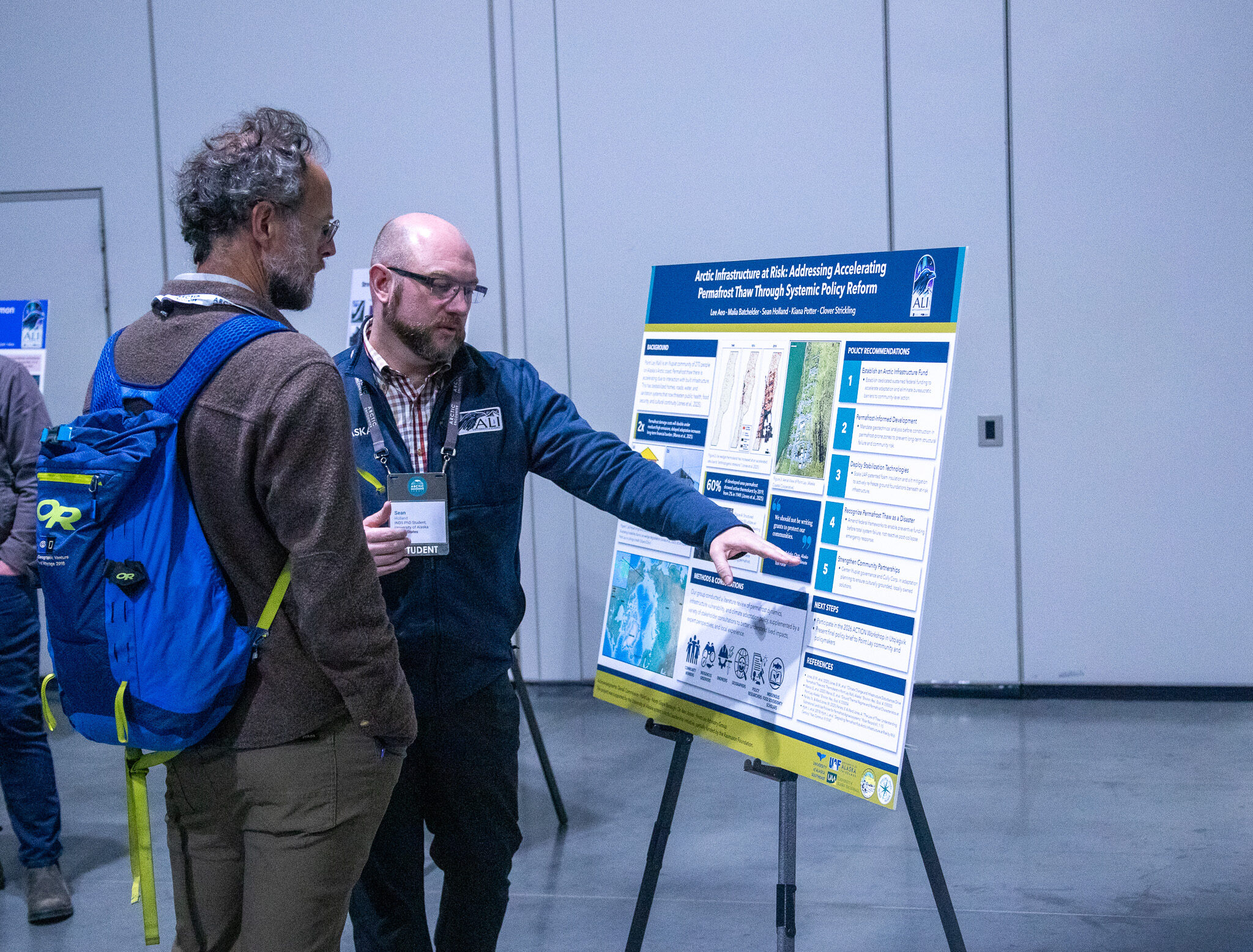 ALI student Sean Holland gestures toward an Arctic Challenge research poster titled 'Arctic Infrastructure at Risk' while explaining it to an attendee at the Arctic Encounter Summit.