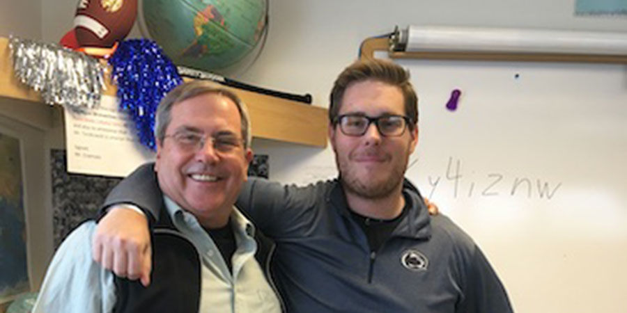 A teacher poses with their arm around the shoulder of an ASMP mentor in a classroom