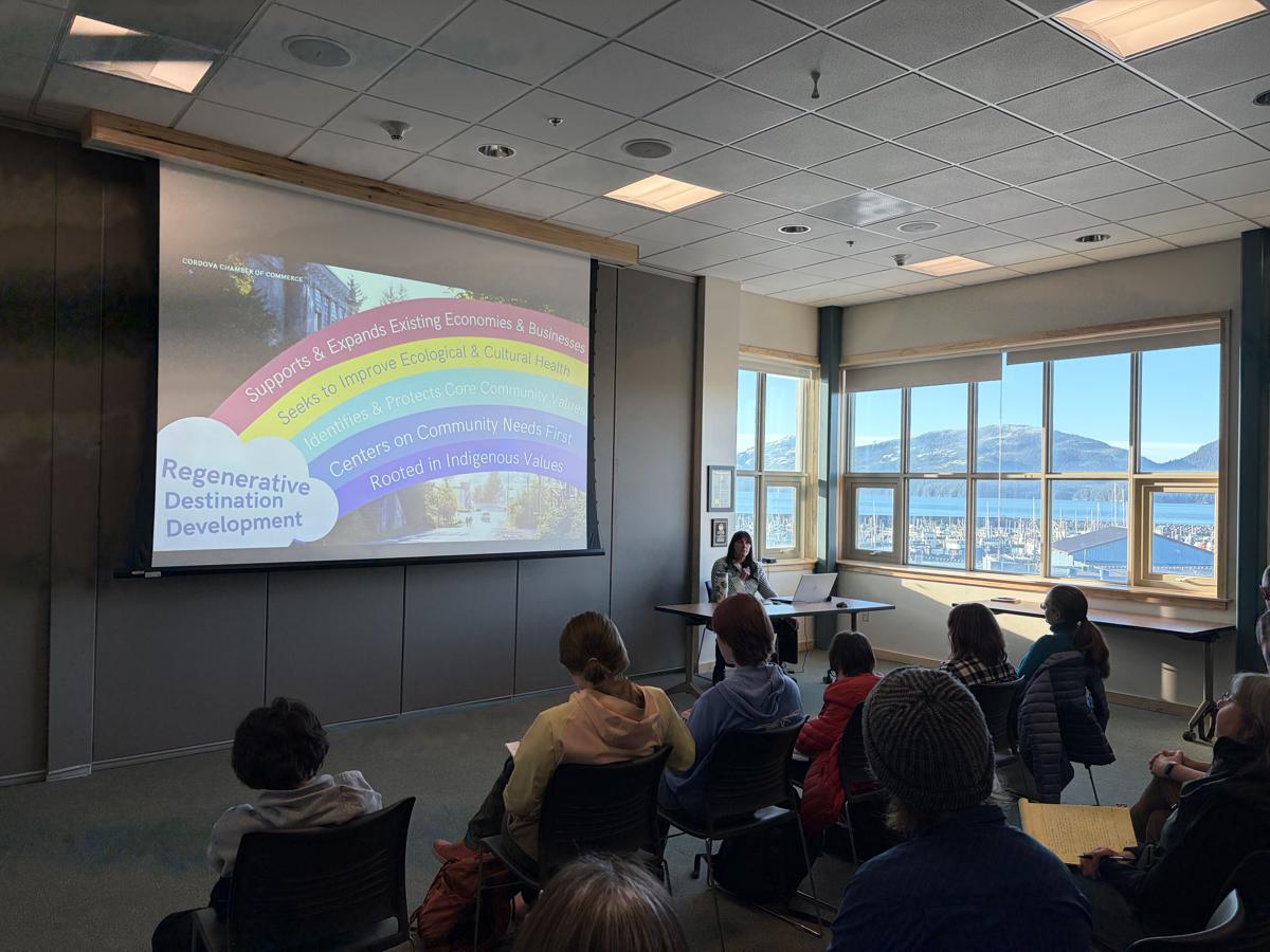 A speaker giving a presentation in a sunlit room full of people of mixed ages.