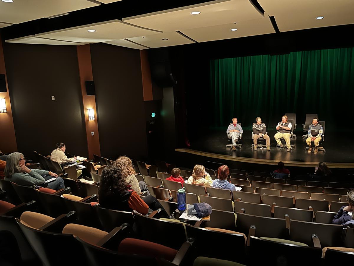 A speaker giving a presentation in a sunlit room full of people of mixed ages.