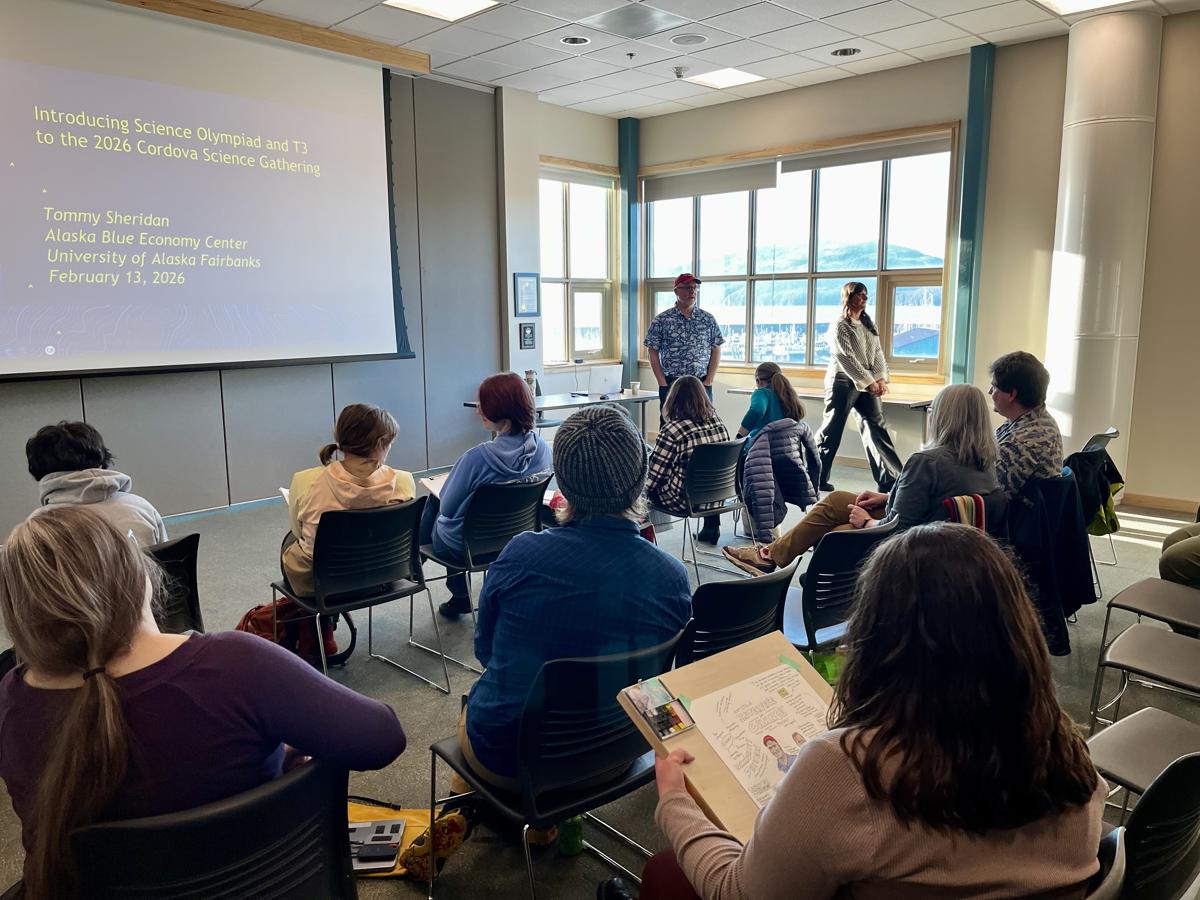 A speaker giving a presentation in a sunlit room full of people of mixed ages.