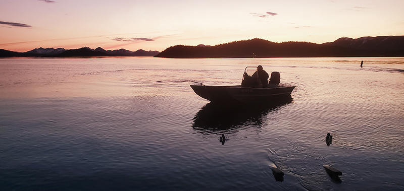 A person on a boat, silhouetted against a sunset in Dillingham, AK.
