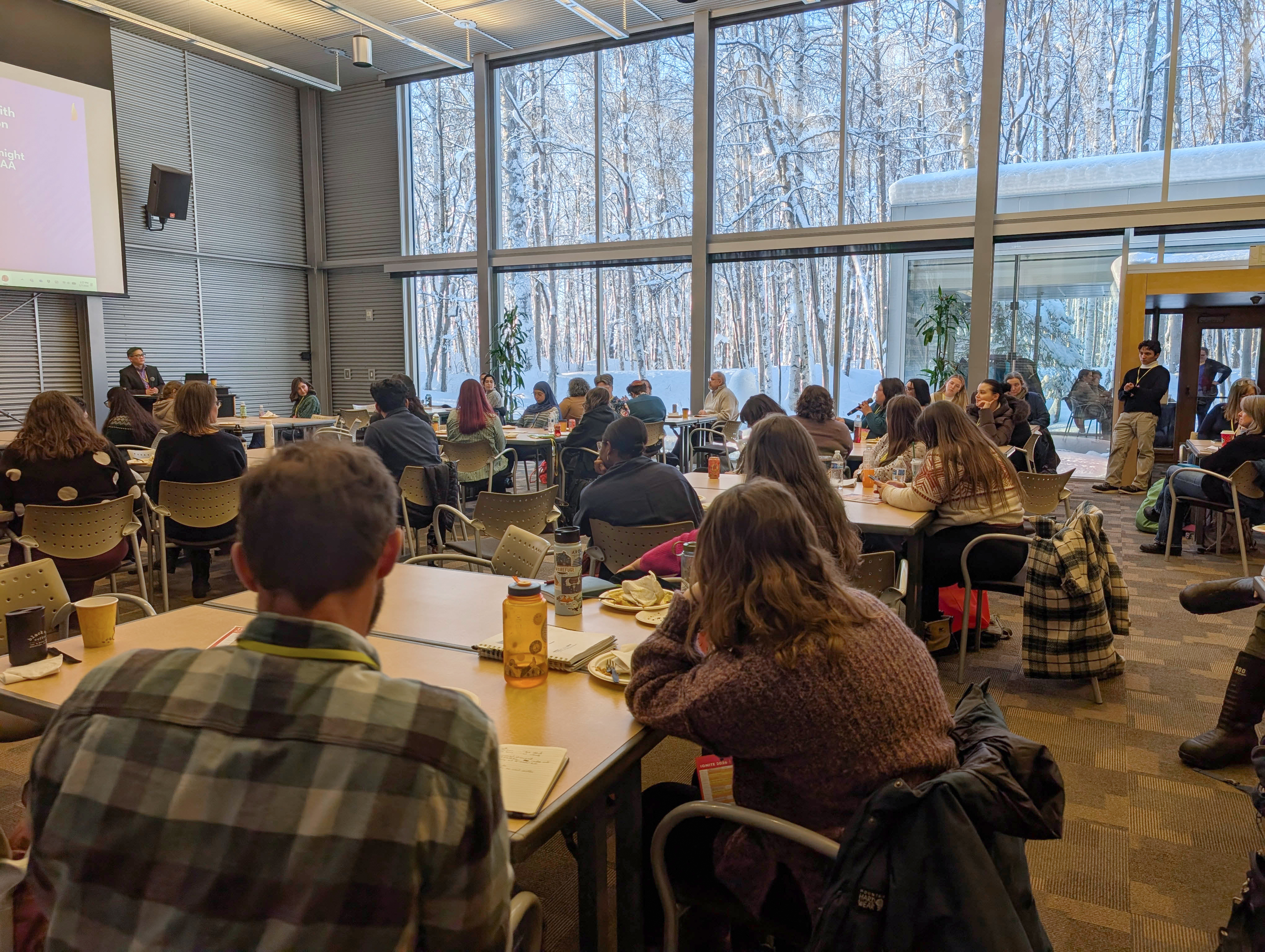 A room full of people at the BP Energy center with birch tree out the window.