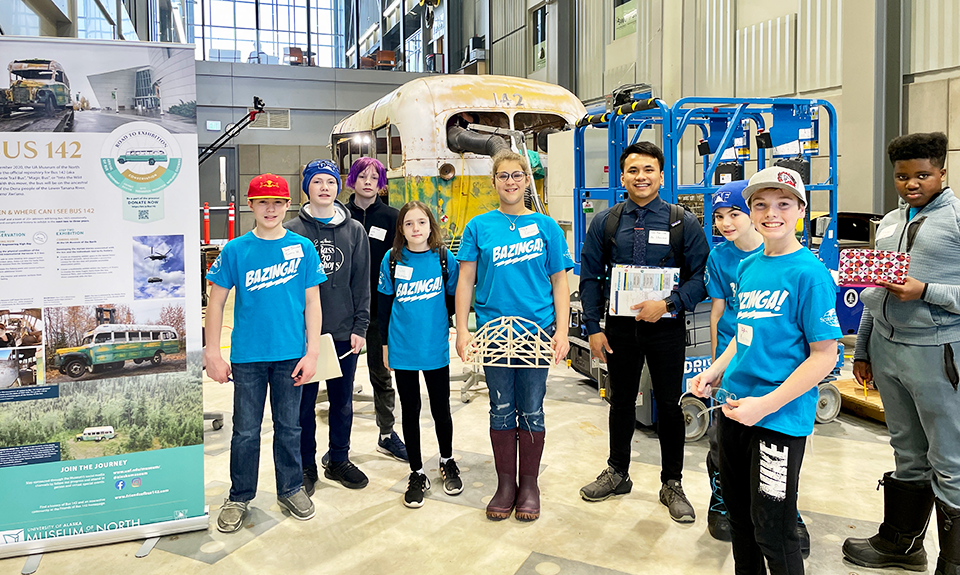 Science Olympiad 2023 winning team "Bazinga!" posing with Bus 142 in the High Bay Structural Testing Lab at UAF's Joseph E. Usibelli Engineering Learning and Innovation Building.