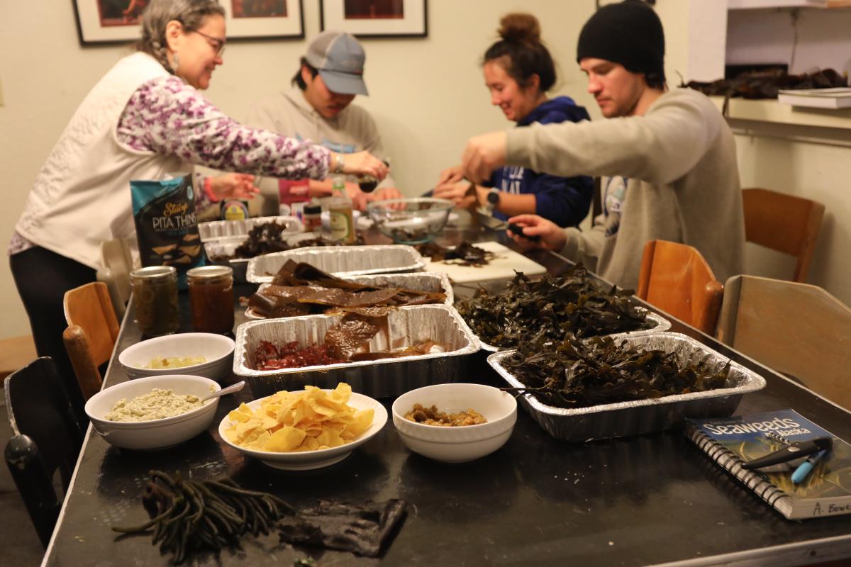 Four people dishing out plates for themselves at a table full of food featuring kelp and seaweed.