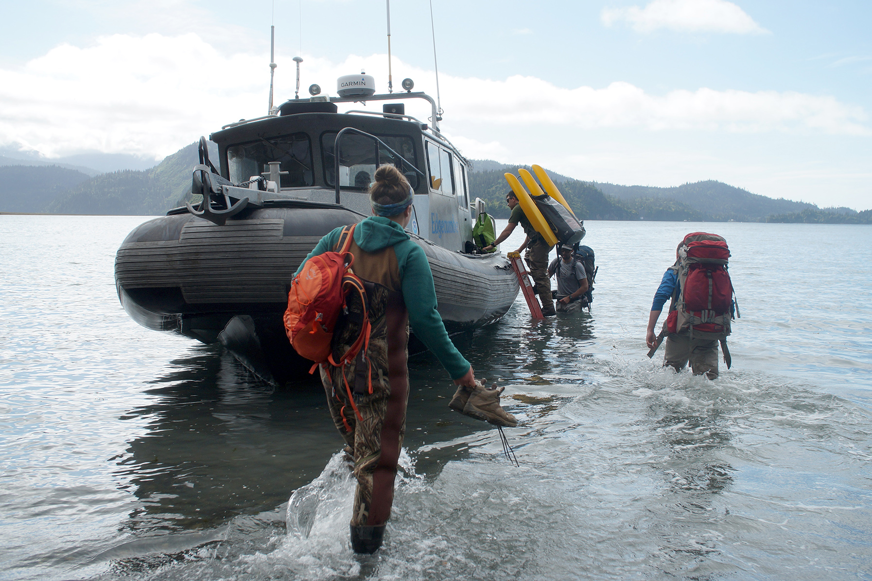 Students with backpacks wade out to a boat.