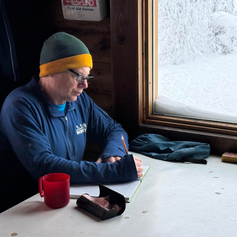 Photo of Ned Rozell writing at a table inside a cabin.