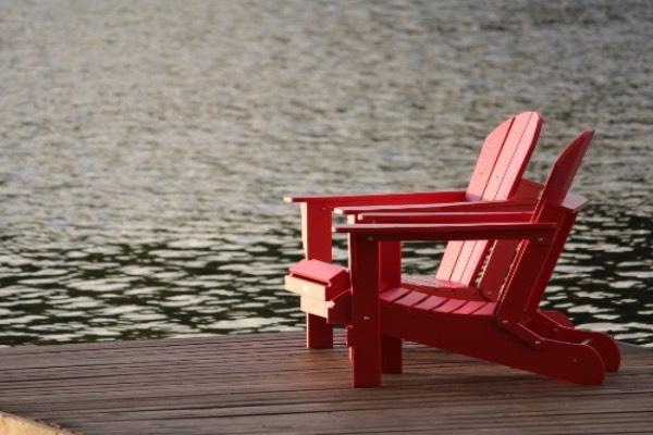 Two red deck chairs on a pier next to lake