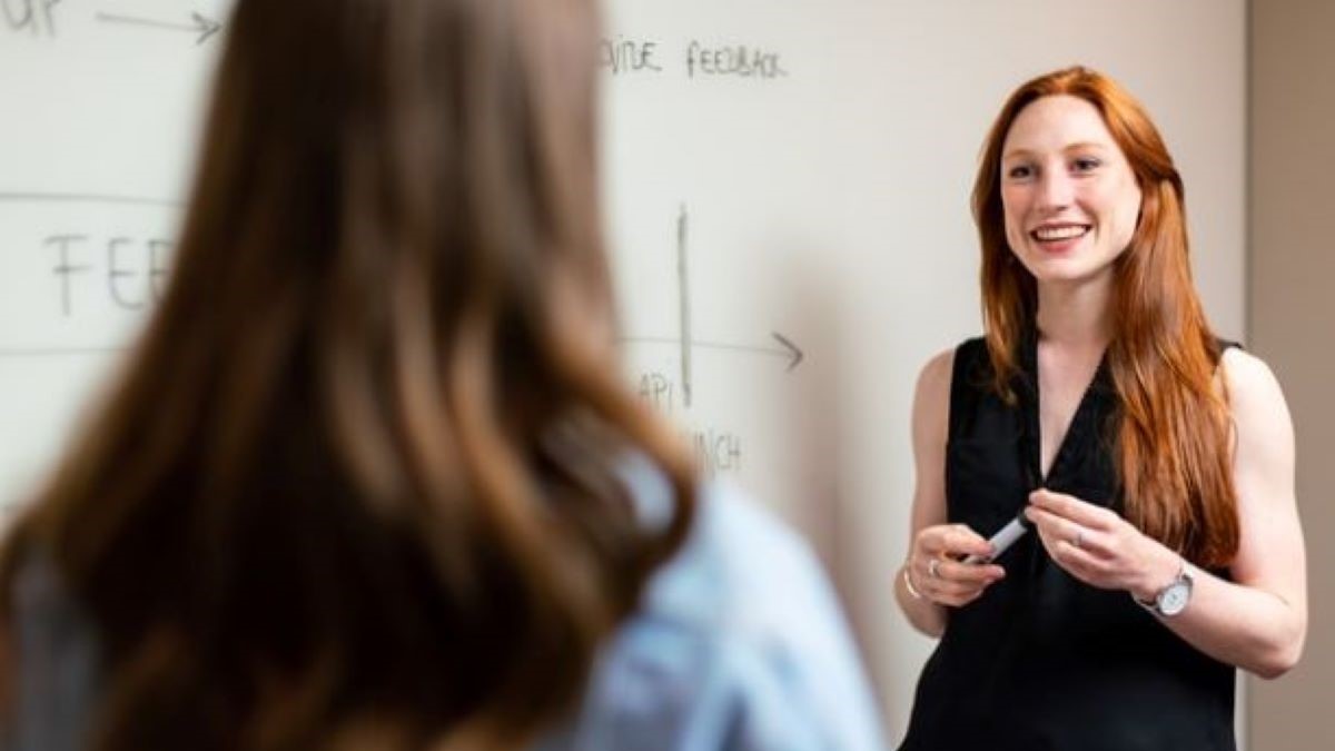 Teacher standing at dry erase board talking to a student.