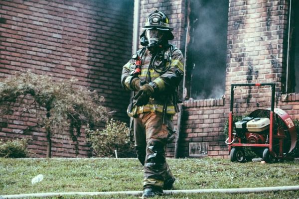 Firefighter standing in front of a brick building that is smoldering.