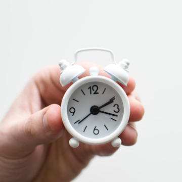Hand holding a white analog alarm clock