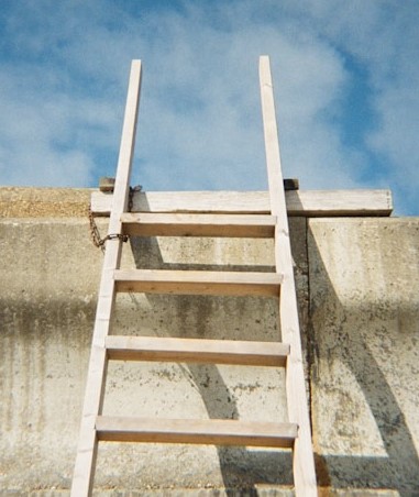 Wooden ladder against buidling leading to roof with a blue sky