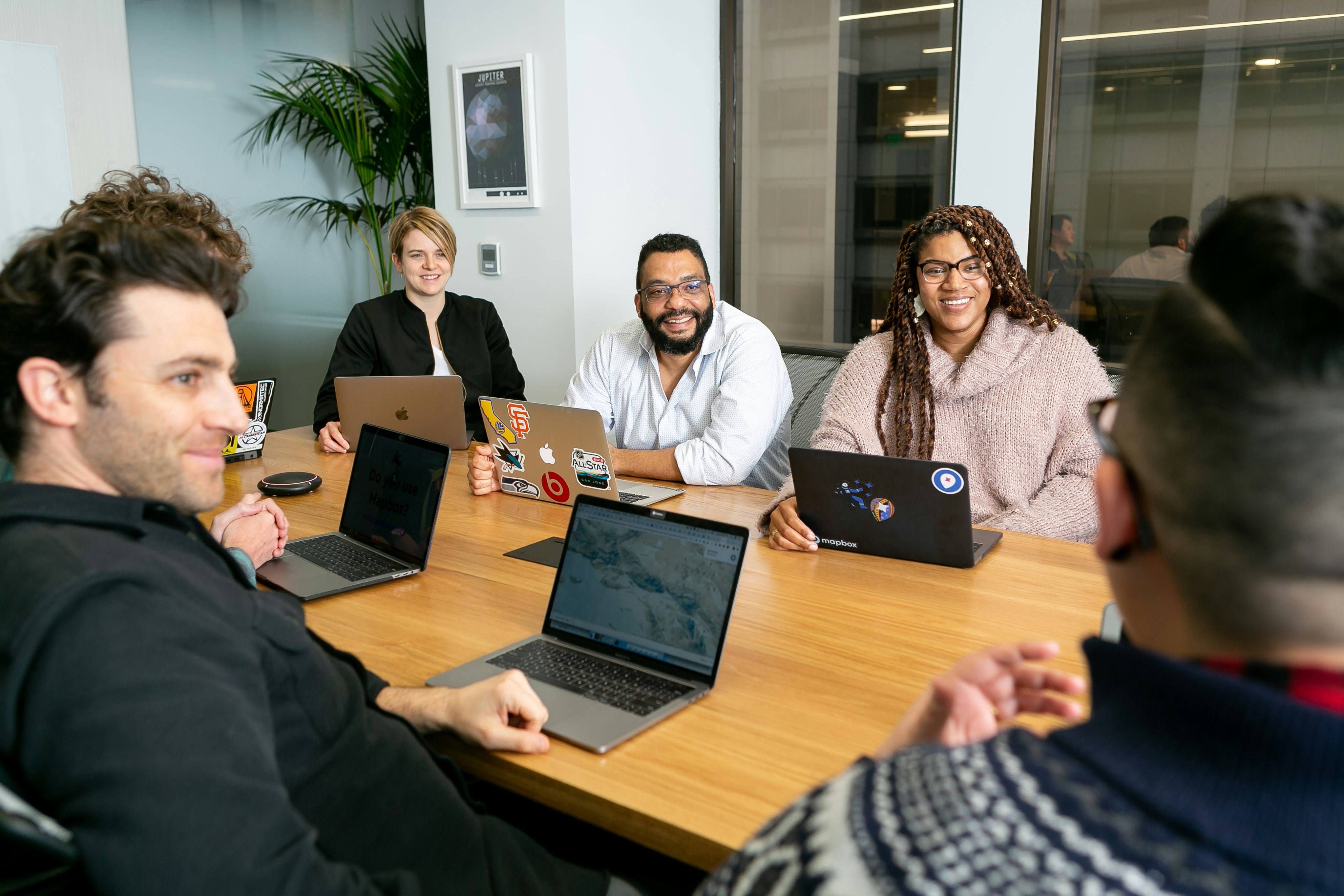 Five people sitting around a wooden table with open laptops.
