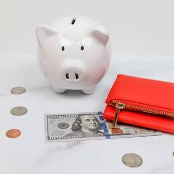 White piggy bank, red wallet, a fake million dollar bill, and some change on a white surface.