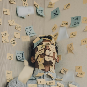 Stressed face covered by yellow and blue sticky notes with tons of work swirling about