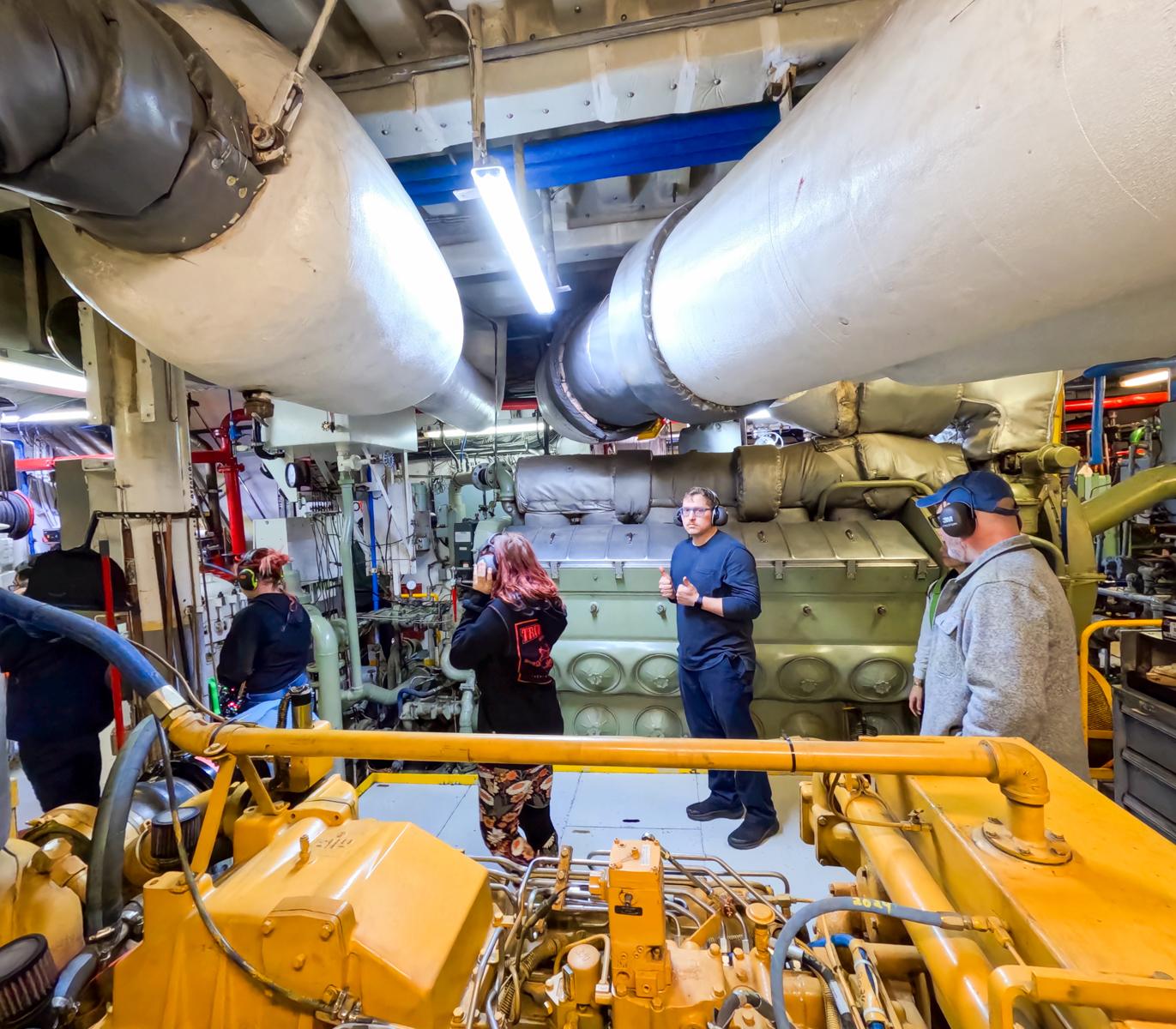 students stand in the engine room of a large ferry vessel