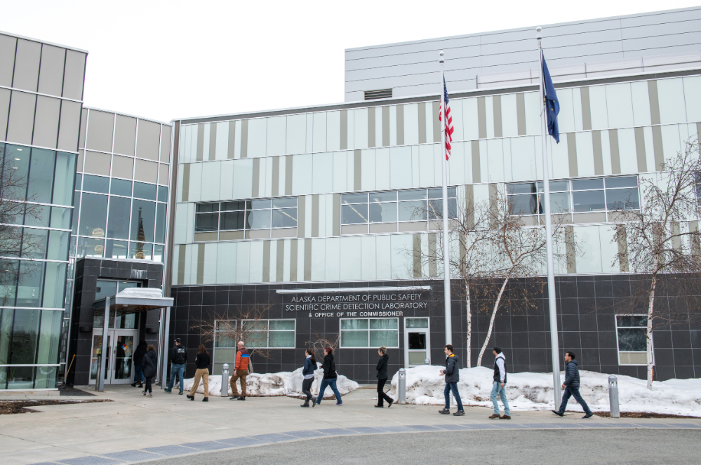 A line of students walks in front of the outside of the Anchorage Crime Lab building