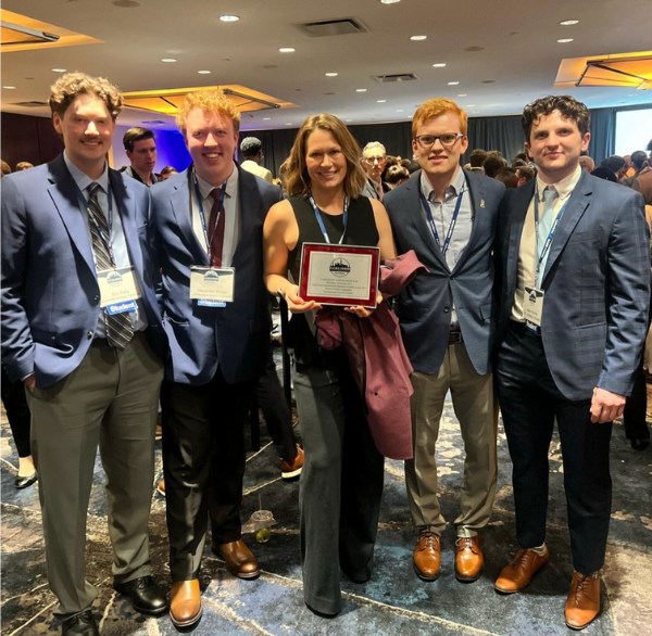 Four young men in suits stand with one woman in the center, holding an award