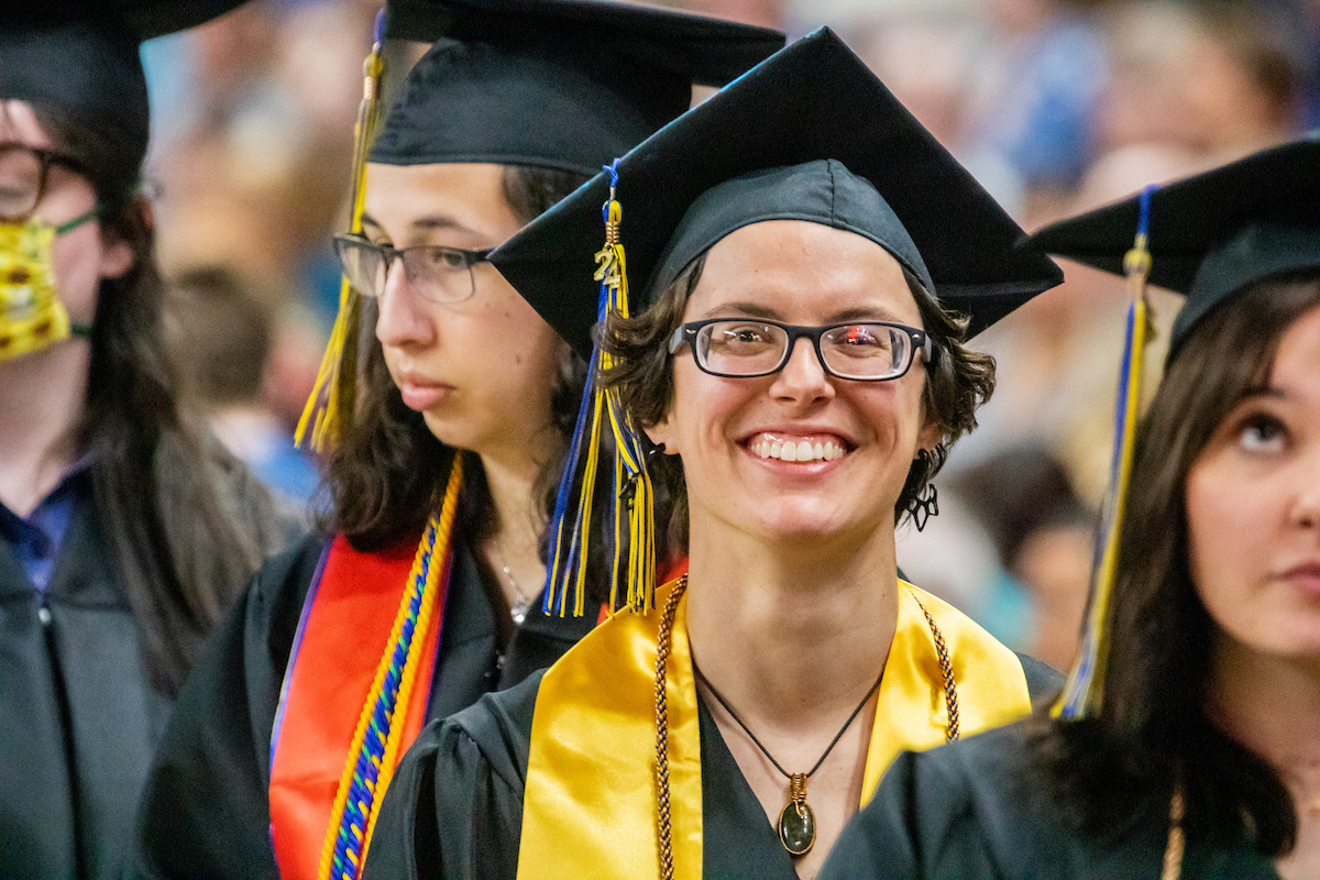 A UAF graduate smiles from the audience wearing their regalia during commencement