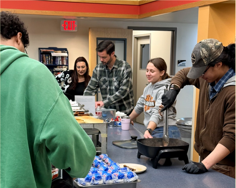 Five people standing around a large counter with breakfast items on it at Prince William Sound College.