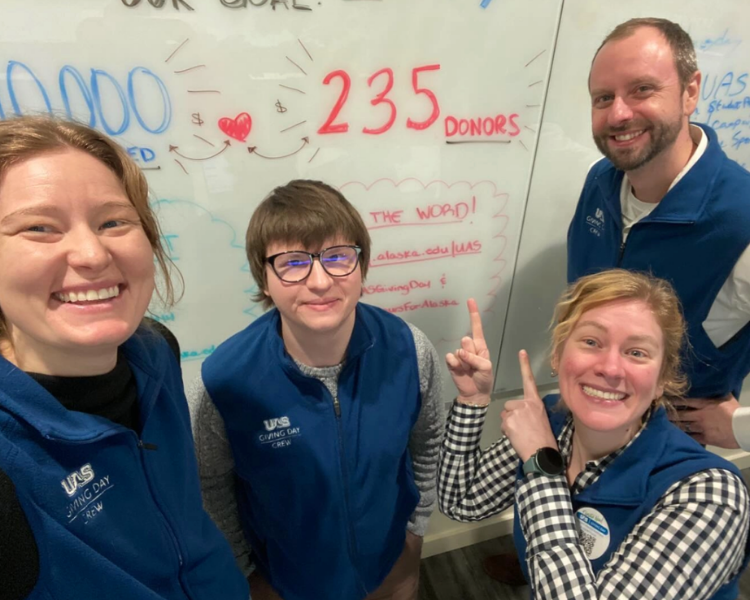 Sabine Hoskinson, Lucas Tempel, Jessey Daws and Chris Natynski standing in front of a whiteboard with UAS Giving Day notes on it.