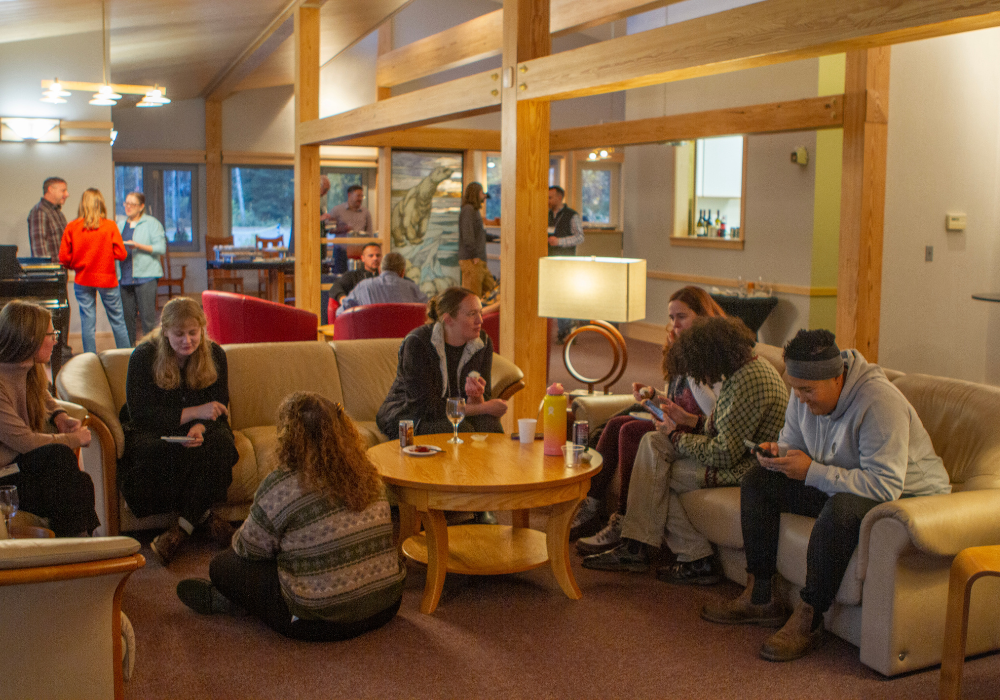 Small groups of people sit and talk in a cozy living room with wood beams and warm lighting during the ALI retreat reception at the UA President’s House.