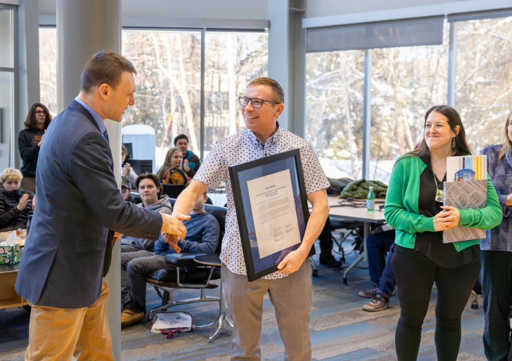 two men exchange a framed paper and shake hands