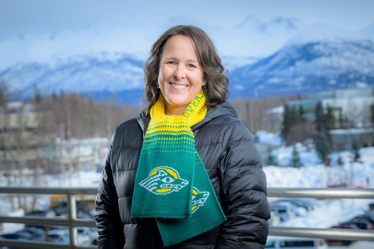 a woman with long brown hair wear a Seawolves scarf with green and yellow and stands in front of a winter background