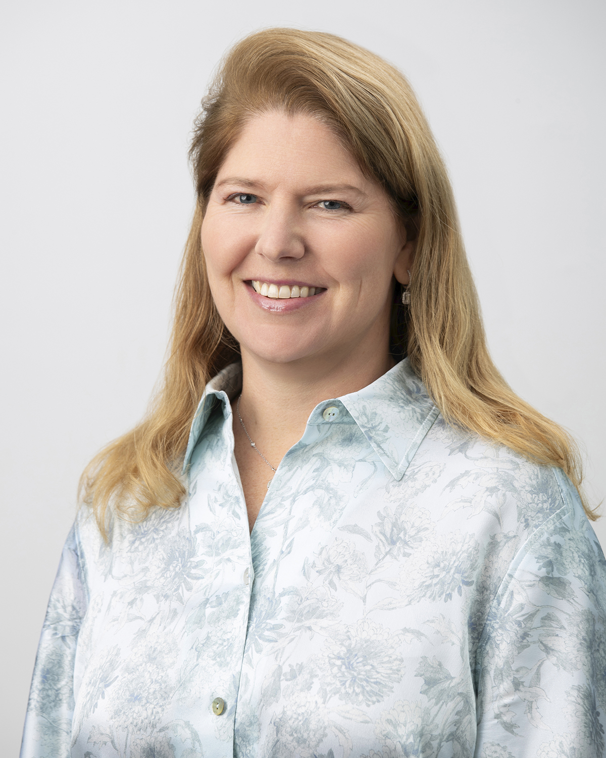 A woman in a white blouse with blonde hair smiles in front of a white background