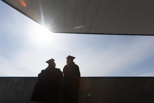 outlines of two graduates in shadow during commencement.