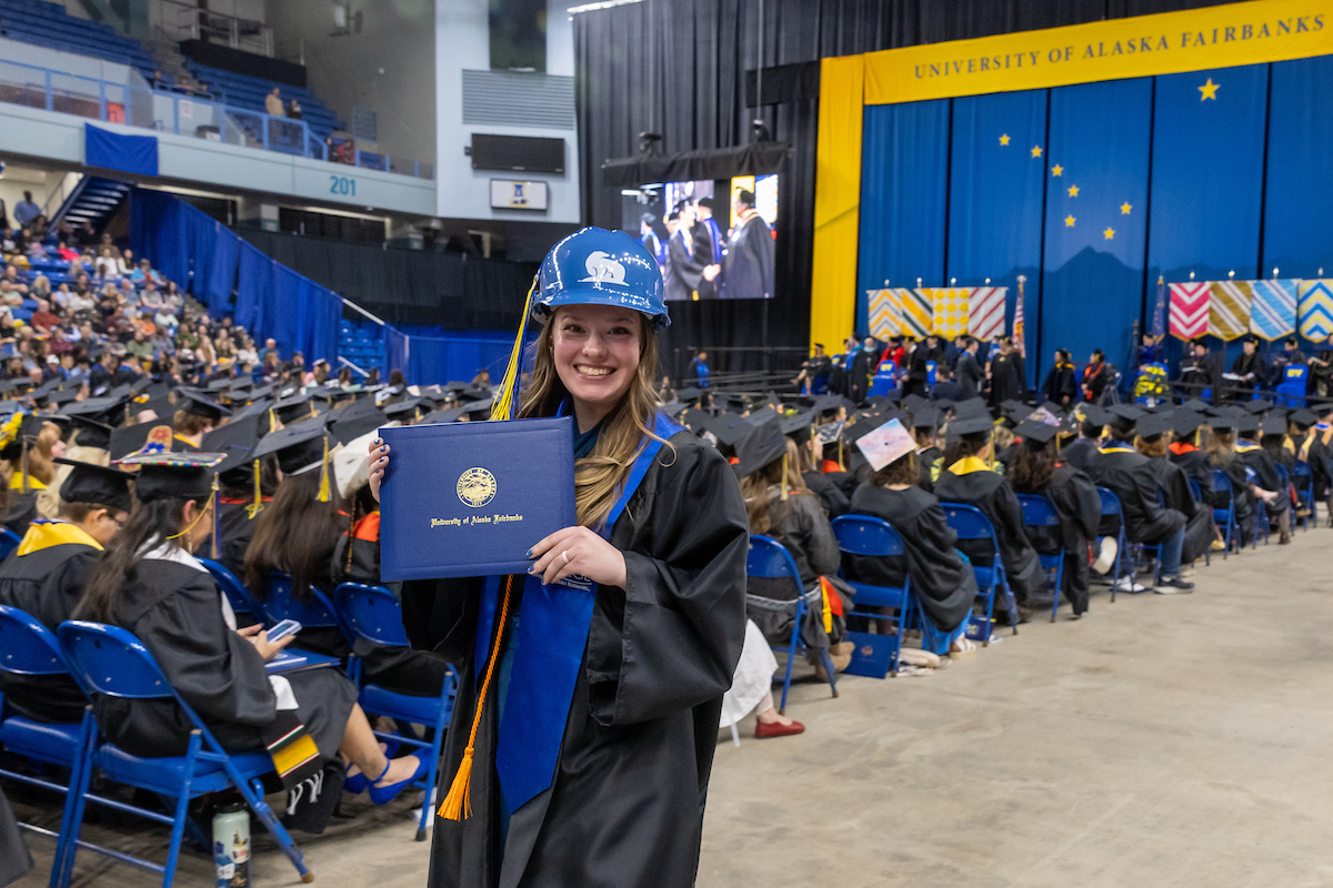 A UAF grad wearing a hard hat leaves the stage with her diploma