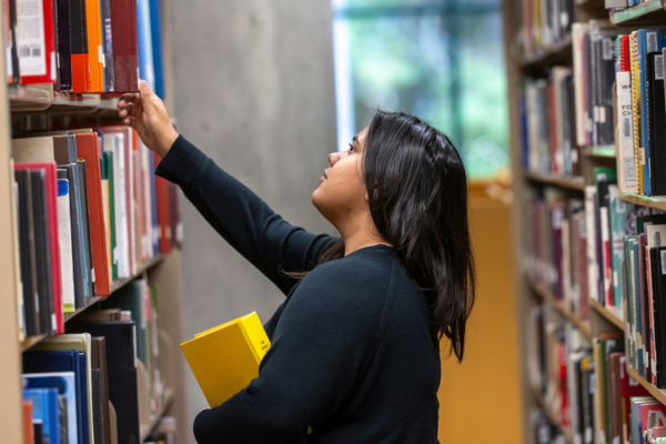 A young female student pulls a book off a library shelf