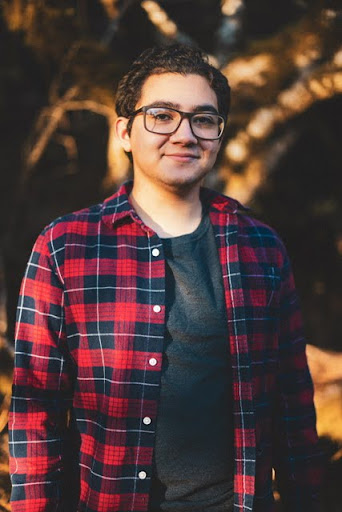 young man with dark hair and a red plaid shirt stands