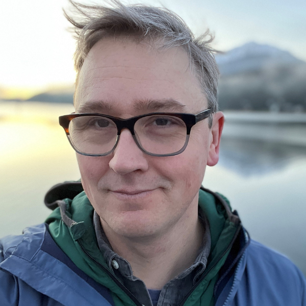 a man with short grey hair in front of water