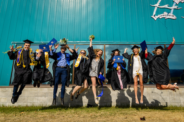graduates wearing regalia jump in the air in unison.