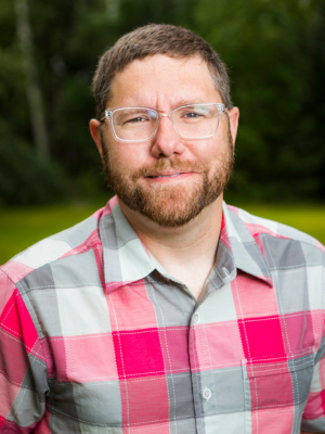 Nate Bauer poses for a portrait in front of a grassy landscape