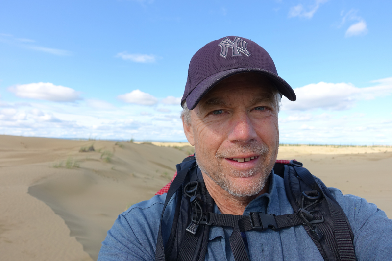 A man with a NY Yankees cap takes a selfie on top of a sand dune