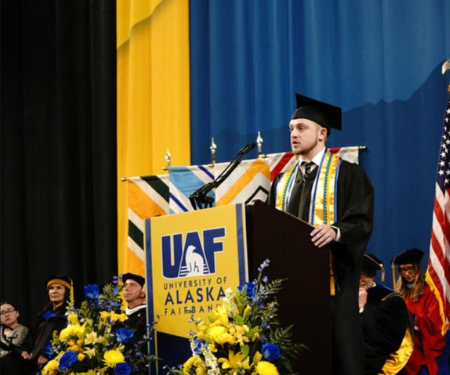  male speaker in regalia stands at podium during ceremony