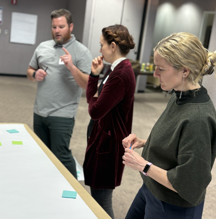 three trainees stand over a table and discuss a problem