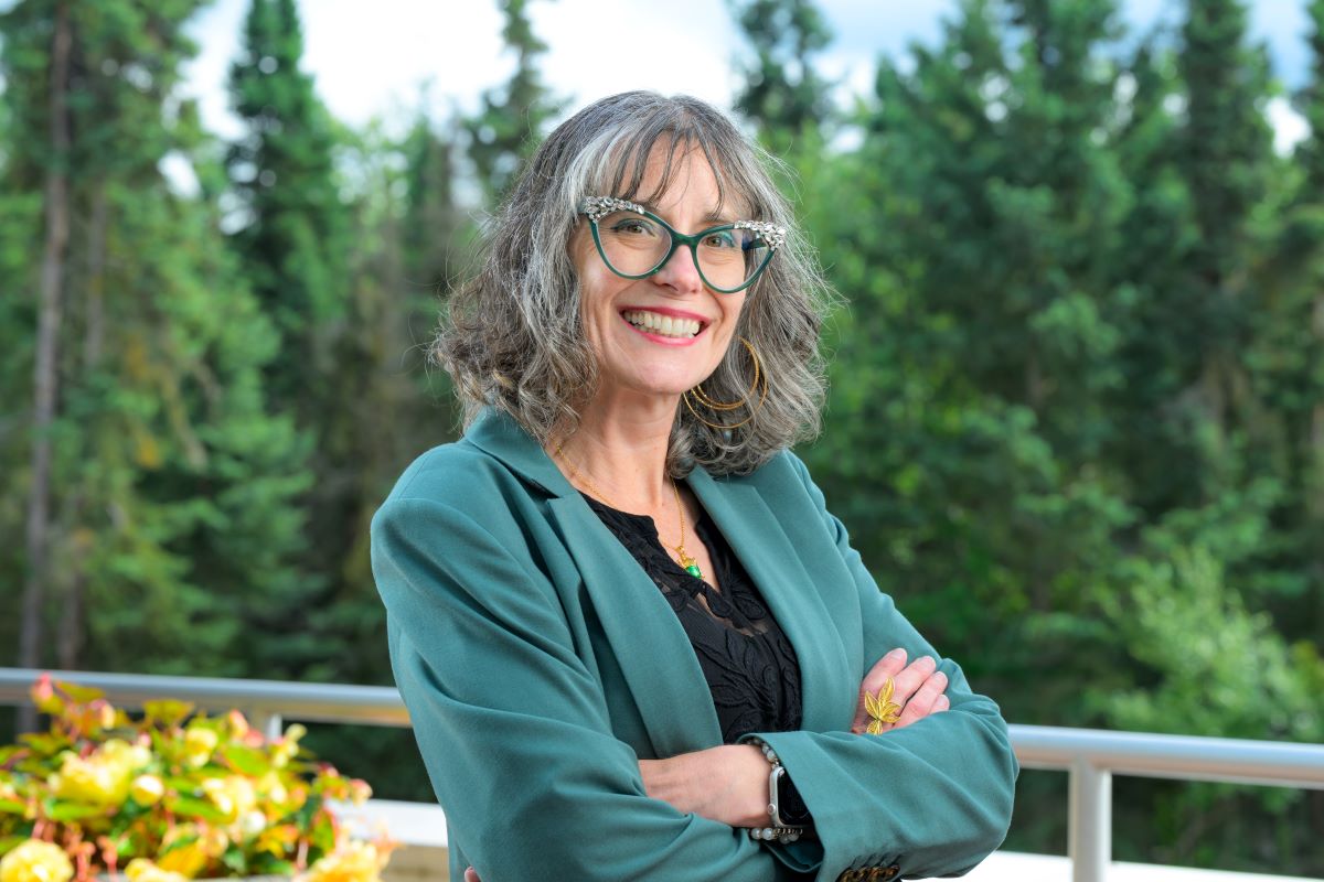woman with grey hair and glasses folds her arms